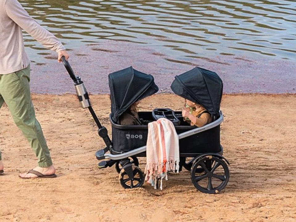 image of dad pulling 2 toddlers inside black BOB Gear Renegade Canopy Stroller Wagon on beach