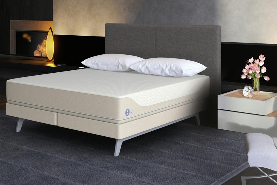 i8 360 Smart Bed in a room with gray floors next to a bedside table with a vase of pink flowers