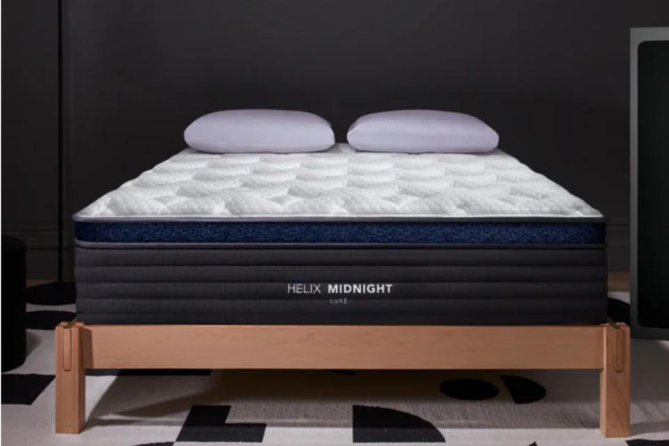 The Helix Midnight Luxe Mattress on a low wood bed frame with two pillows on top.