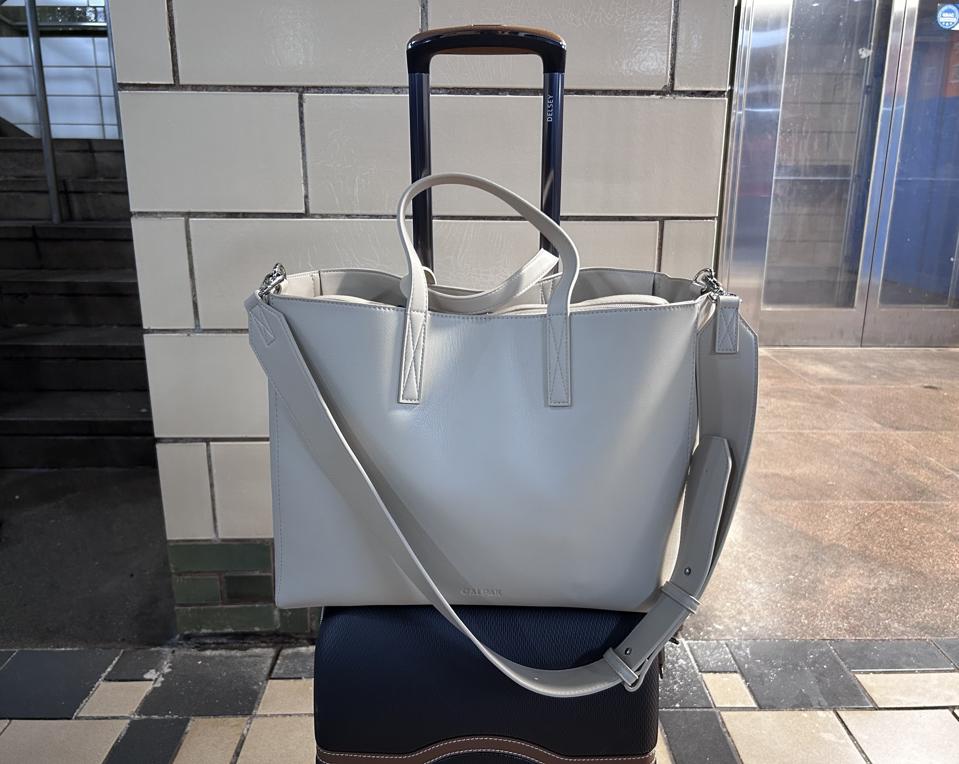 Calpak Haven Laptop Tote secured to a suitcase in a subway station 