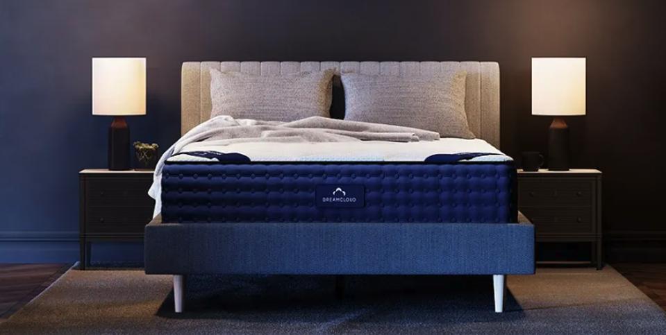 DreamCloud Hybrid Mattress (Queen) on a gray fabric bed frame in a dark blue room