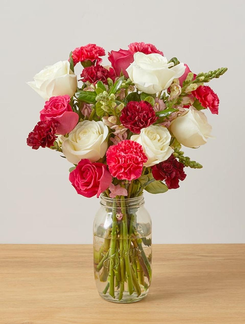 The Bouqs Co. Flower bouquet white red pink blooms green stems in water clear jar