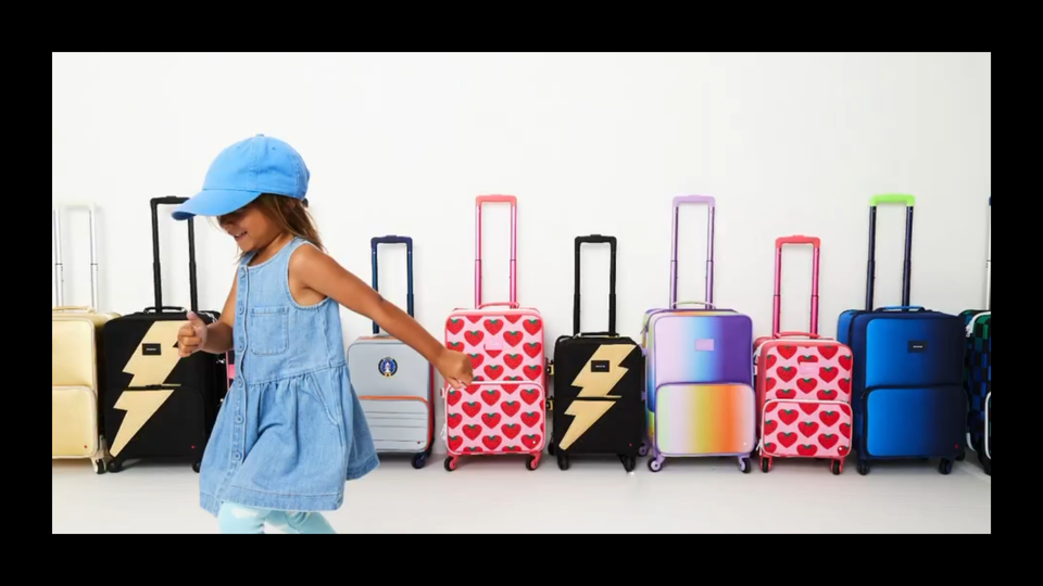 A little girl runs in front of a lineup of State suitcases with wheels. 