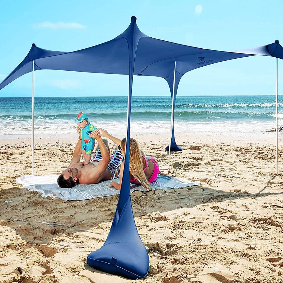 A blue beach canopy in the sand with a couple and baby sitting underneath