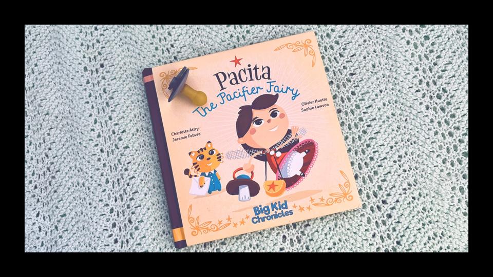 The book "Pacita: The Pacifier Fairy" on an knit baby blanket with a pacifier.