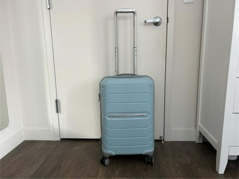 A light blue suitcase against a white door.