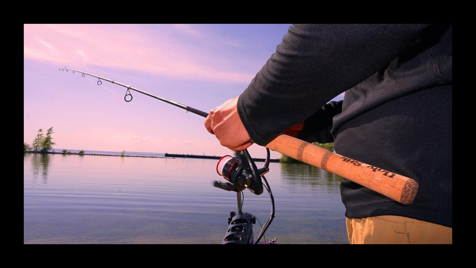 A person using the Ugly Stik Elite Spinning Rod on a lake at sunset.