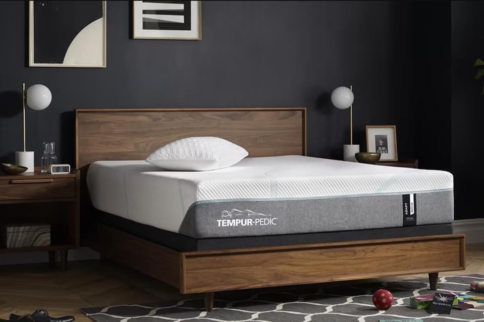 A Tempur-Pedic Tempur-Adapt mattress on a walnut-colored mattress frame in gray room. 