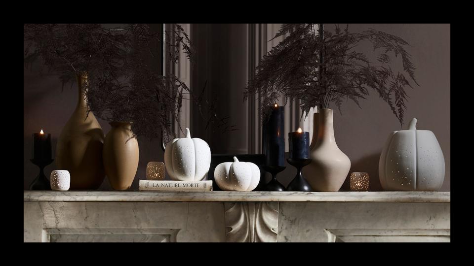 A mantel with fall and Halloween decorations like white ceramic pumpkins and black candles