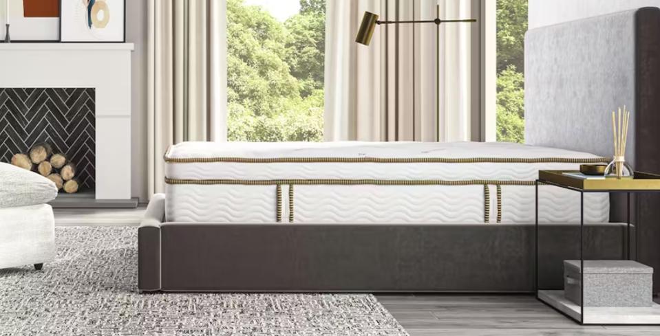 The Saatva Latex Hybrid from the side on a bed frame in front of two windows in a bedroom