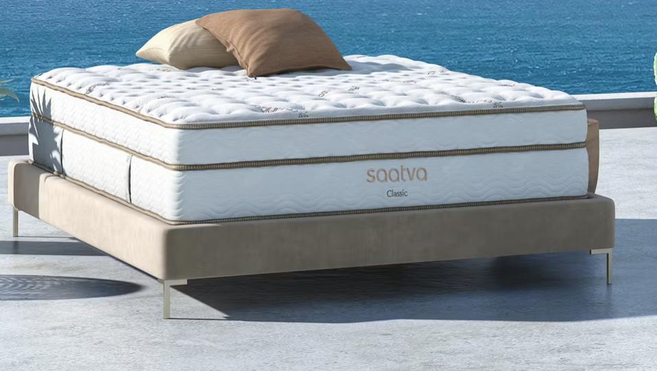 The Saatva Classic mattress on a low beige bed frame with a body of water in background.