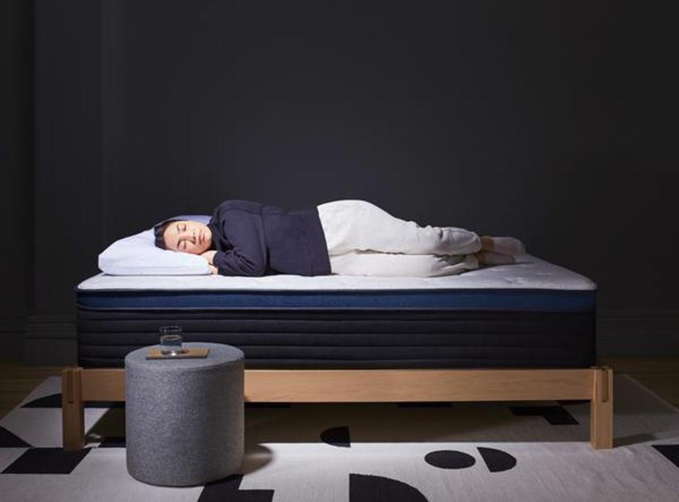 A person lying on the Helix Midnight LUXE Hybrid Mattress in a darker room