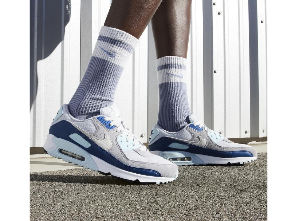 photo of man's feet wearing blue & white Air Max 90s outside on gravel w/ nike socks