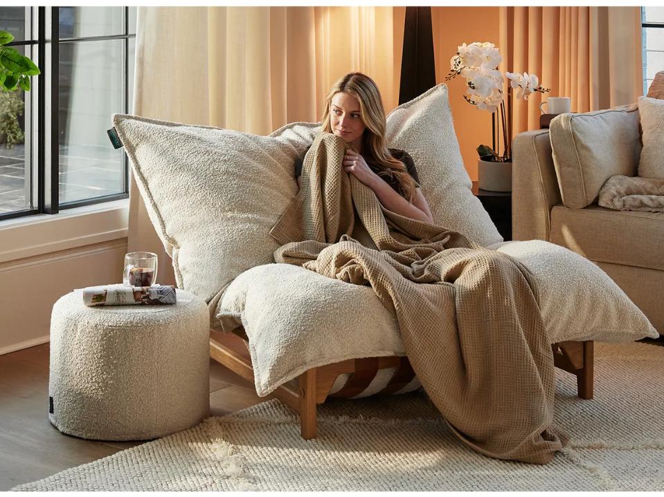 woman on beige lovesac accent chair using light brown waffle weave footsac blanket daytime