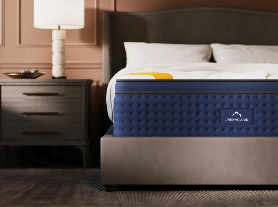 The DreamCloud Premier Rest Hybrid sitting in a bedroom next to a nightstand.