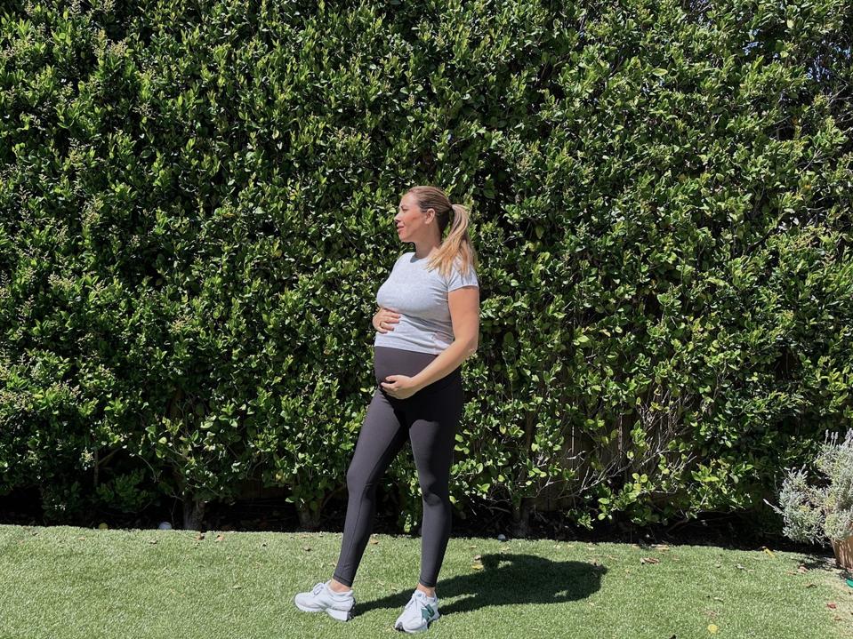 Author wearing the Old Navy maternity leggings on the grass, cradling her bump.