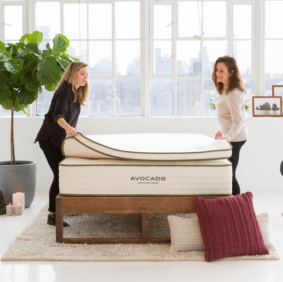 Two women placing the best cooling twin xl mattress topper on top of an Avocado mattress. 