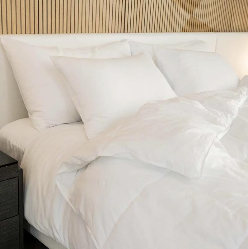 A bed with pillows and the FluffCo down alternative comforter against a tan wall