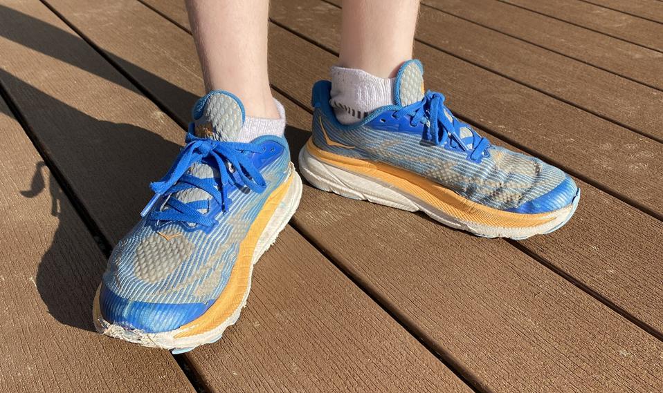 A pair of blue and orange Hoka shoes on a kid's feet. 