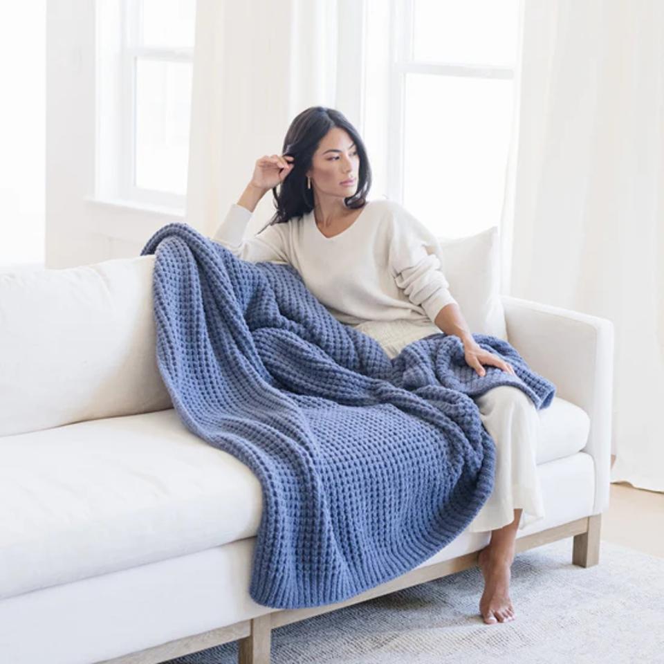 A woman sitting on a white couch with the Saranoni Waffle Knit XL Throw in blue