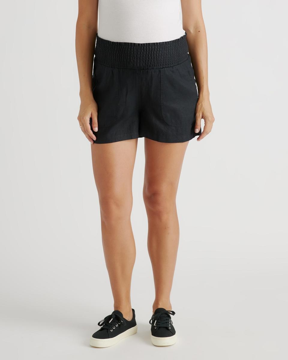 A white woman wearing the Quince 100% European Linen Maternity Shorts on a pale background