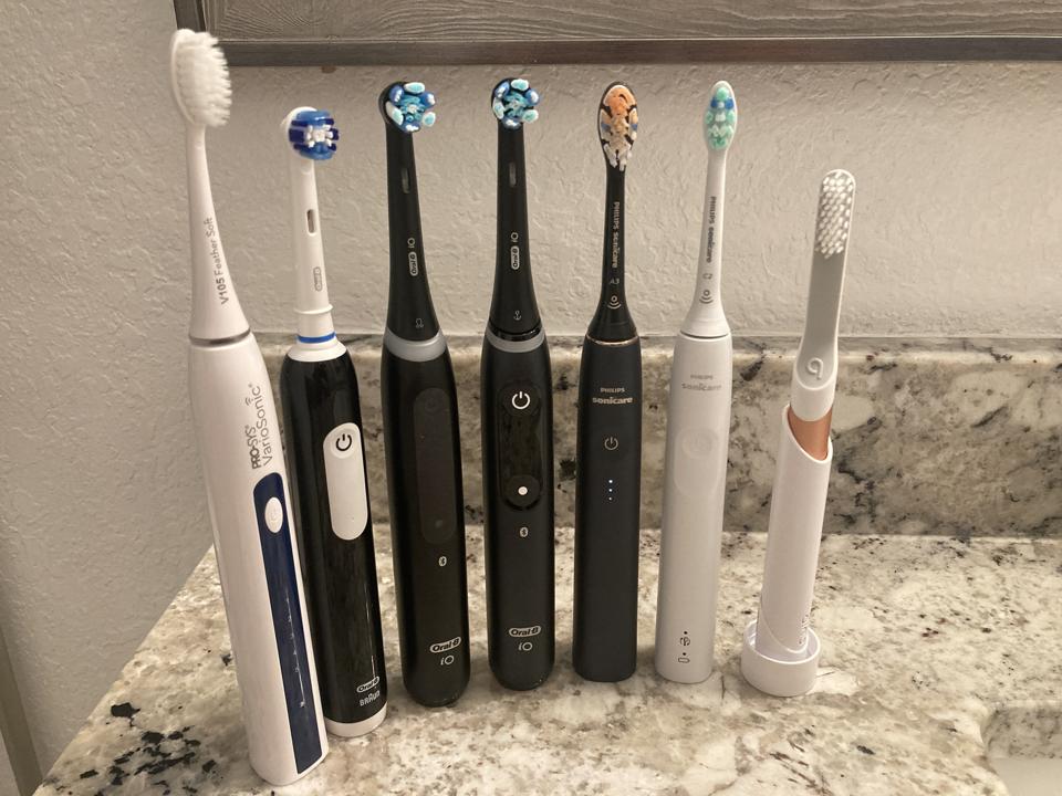 Seven electric toothbrushes lined up in a row on a bathroom countertop