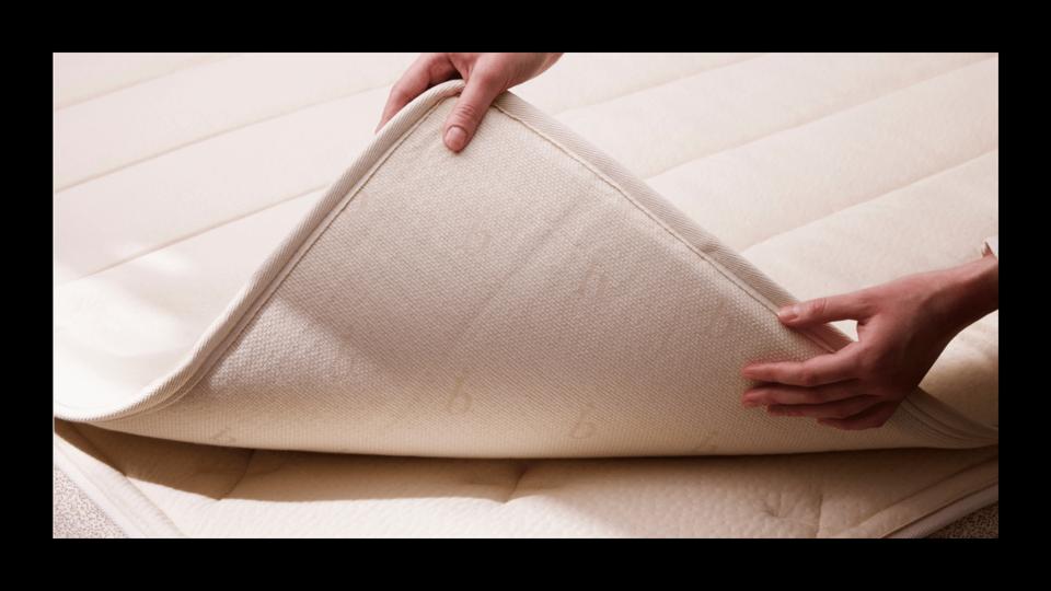 A person showing the corner of a mattress topper on top of a mattress