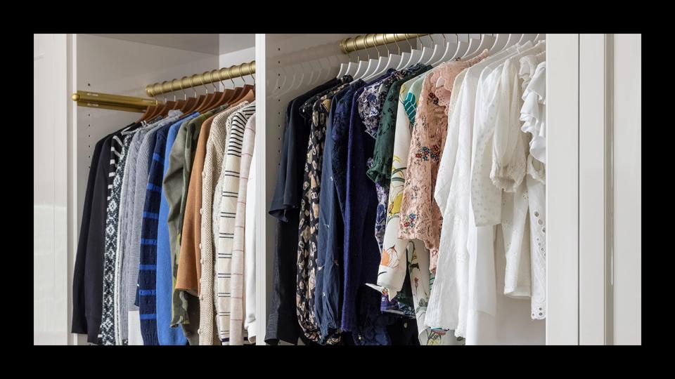 A closeup of clothes hanging neatly in a white closet with a gold rod.