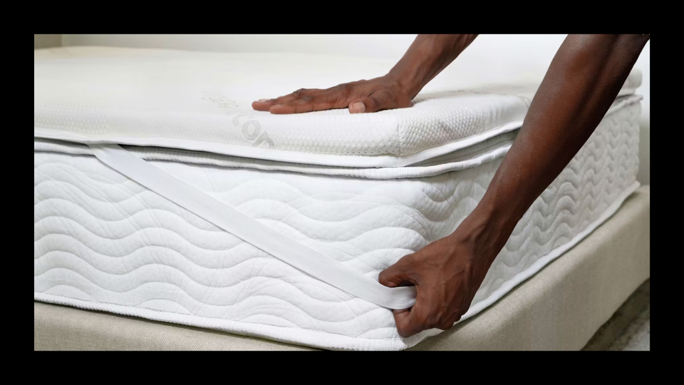 A person's hands strapping a topper to a bed.