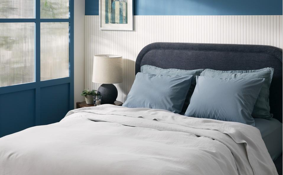 The Parachute Percale Sheets in blue on an upholstered bed frame in a blue and white room.