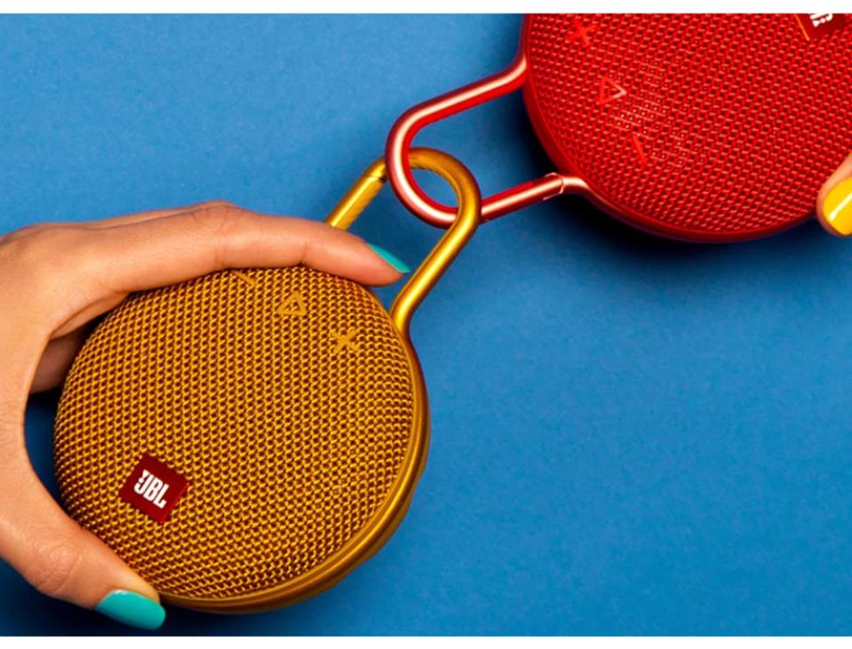 2 JBL Clip 3 waterproof speakers, yellow and red attached with nail-polished hand on blue bg