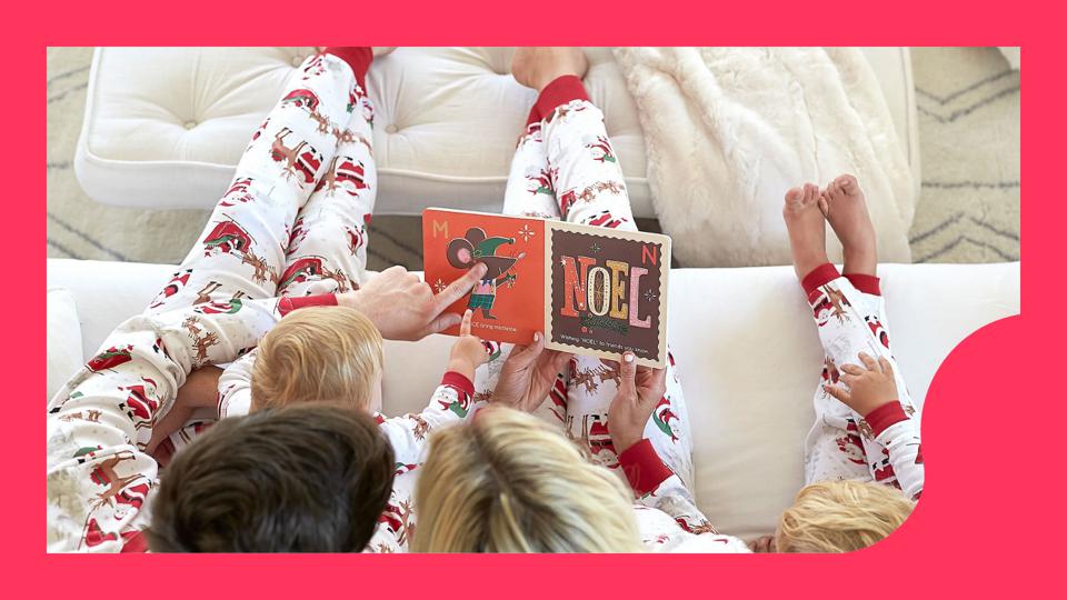 Family of 4 on the couch reading a book in matching Christmas pajamas. 