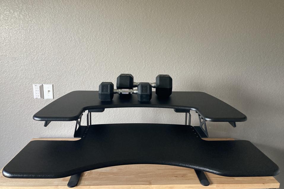 Black VariDesk Pro Plus 36 with two hand weights on it with a gray wall behind it