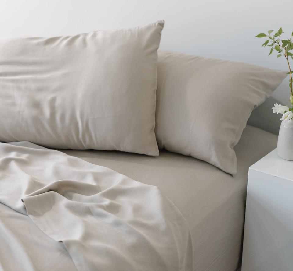 Cozy Earth sheets on mattress with pillows next to bedside table with bud vase.