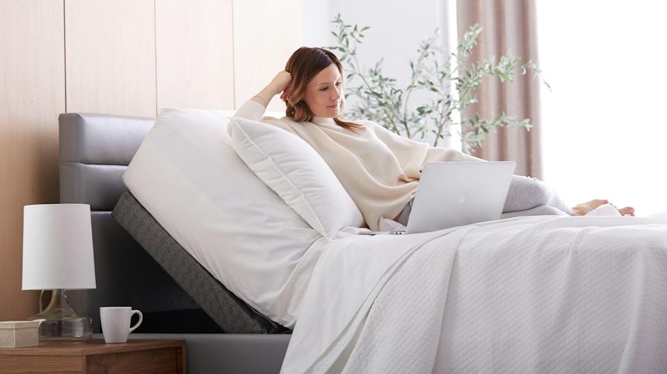 A woman reading her laptop on the Saatva Adjustable Base Plus