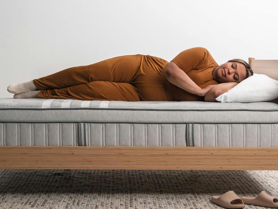 Woman lying on her side on the Leesa Plus Hybrid Mattress on a wooden bed frame.