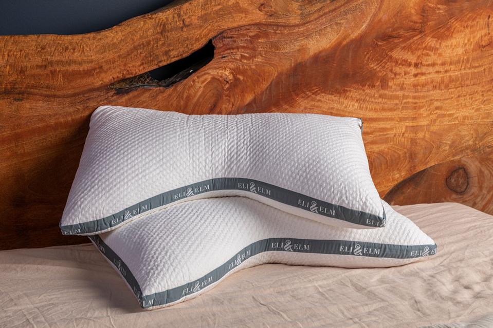 Two Eli & Elm Cooling Side-Sleeper Pillows stacked on mattress and leaning against wooden headboard.