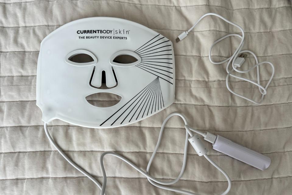 CurrentBody LED Mask, USB cable and controller laid against white bedspread