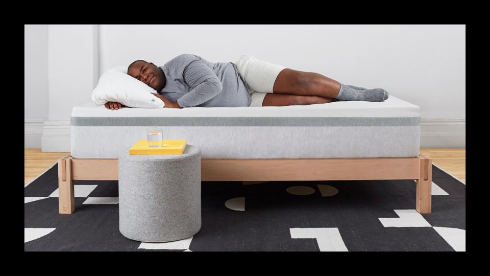 A man lying on the Helix Plus Mattress facing the camera on a bed frame with black border