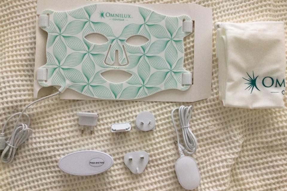 Omnilux Contour Face mask and assorted accessories against white bedspread