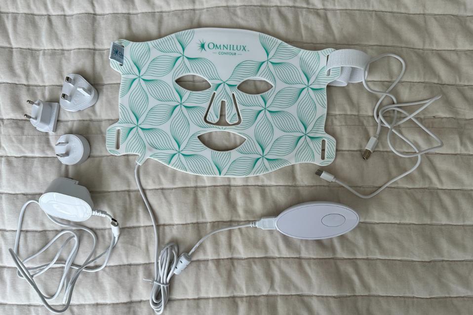 Omnilux Contour Face mask and accessories laid out against white bedspread