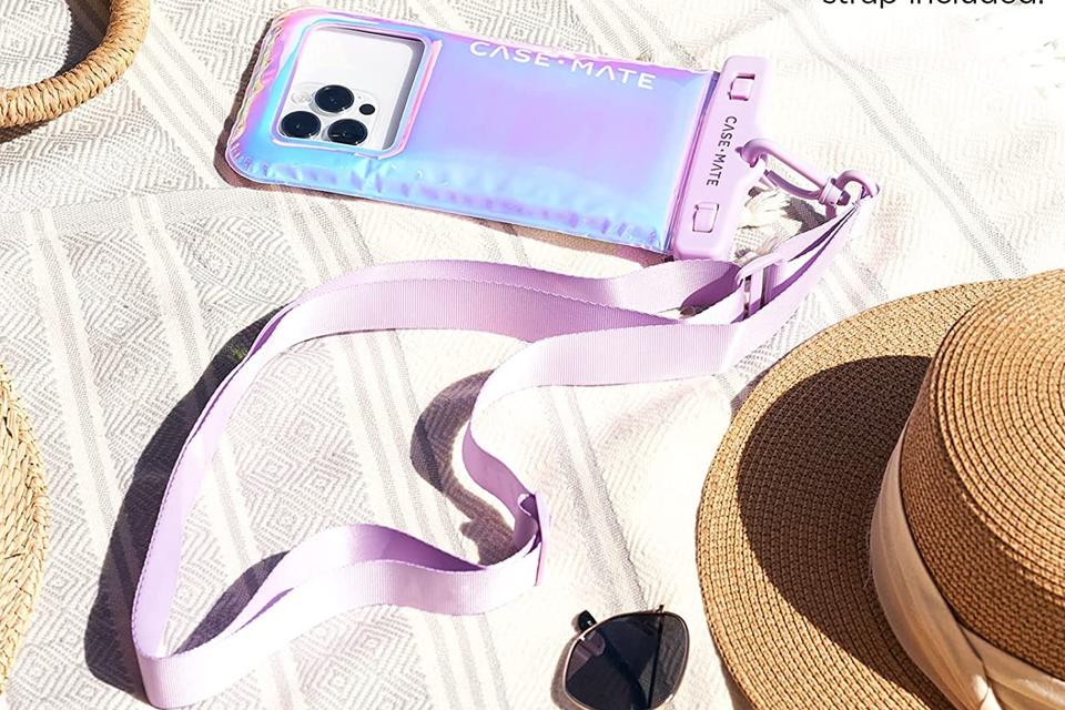 The Case-Mate Waterproof Floating Pouch lying on a beach blanket near a hat and sunglasses