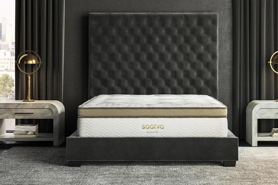 Saatva HD Mattress on dark upholstered frame with tall headboard in bedroom.