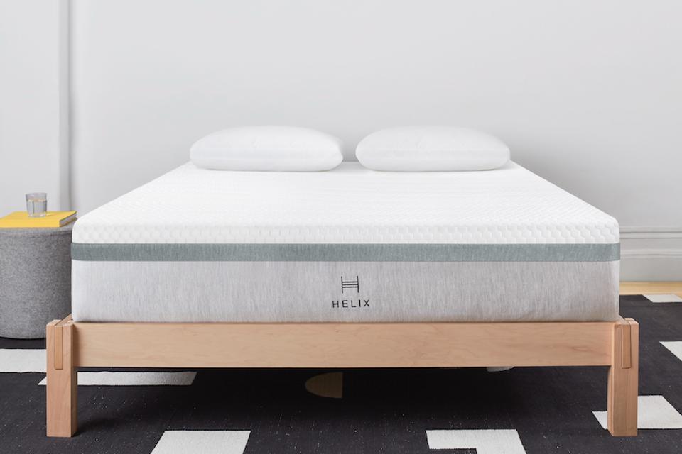 The Helix Plus mattress on wooden frame next to bedside table.