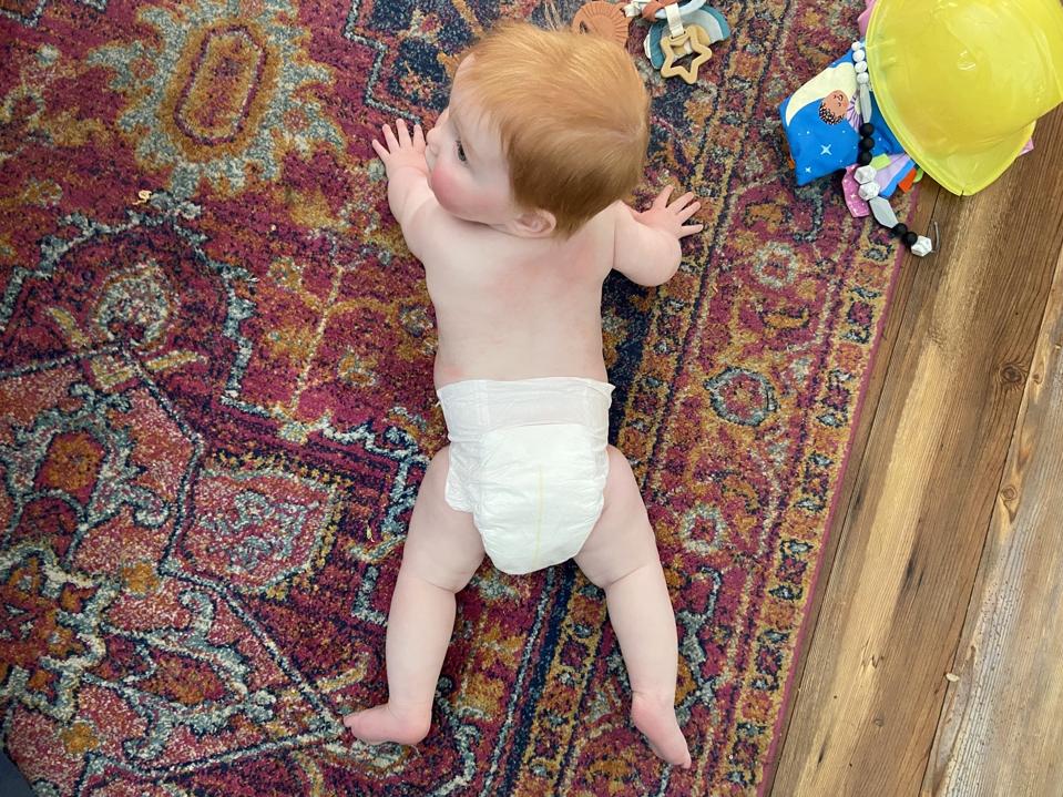 A baby wearing the Bambo Nature Dream Diaper on a multicolored rug.