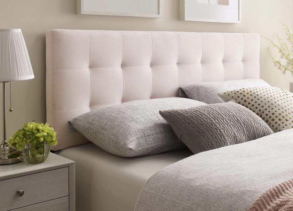 A pink headboard up against a wall with a nicely made bed up against it. 