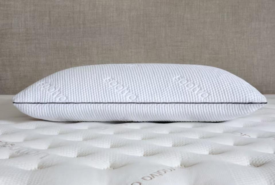 The Saatva Graphite Memory Foam Pillow on top of a mattress against a beige wall