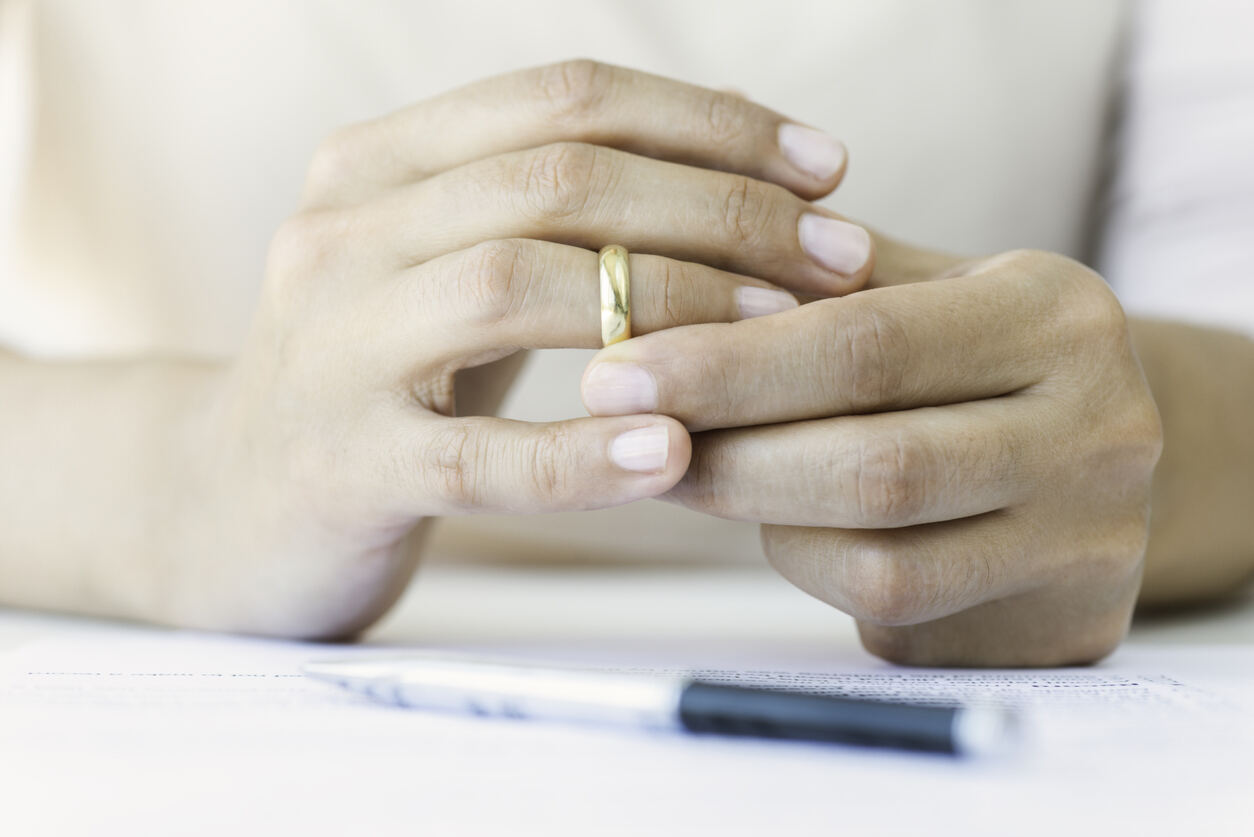 gros plan sur les mains d'une femme retirant son alliance avec les papiers du divorce et un stylo sur la table