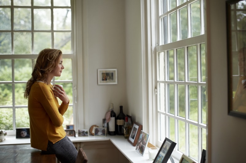 femme dans la cuisine regardant par la fenêtre la nature environnante