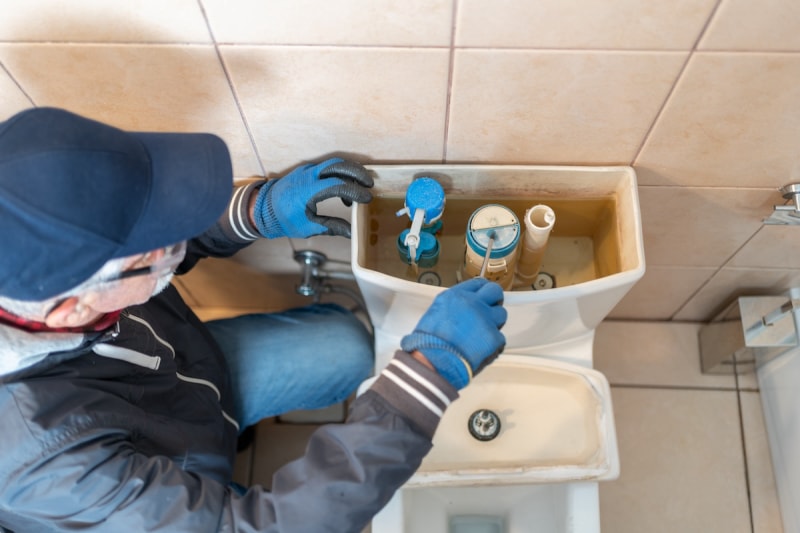 Un plombier nettoie le robinet d'arrivée d'une toilette.